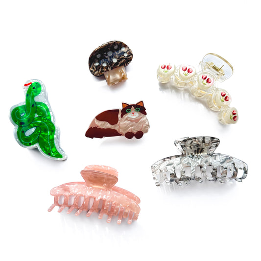 Set of novelty hair clips including a snake, mushroom, cat, and other designs on a white background.